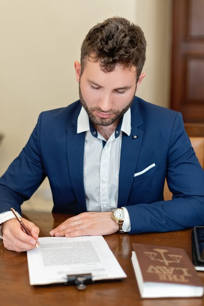 A businessman in formal attire signs a legal document at an office desk, emphasizing professionalism.